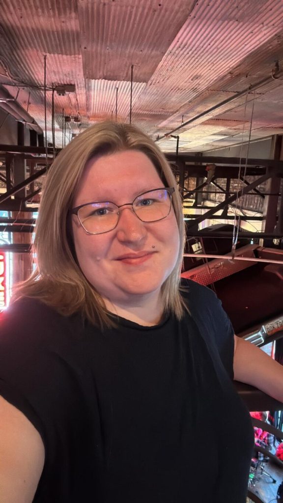 Eine Frau mit blonden Haaren und Brille lächelt in einer Innenraumkulisse in die Kamera. Eine Frau mit blonden Haaren und Brille lächelt in einer Innenraumkulisse in die Kamera.